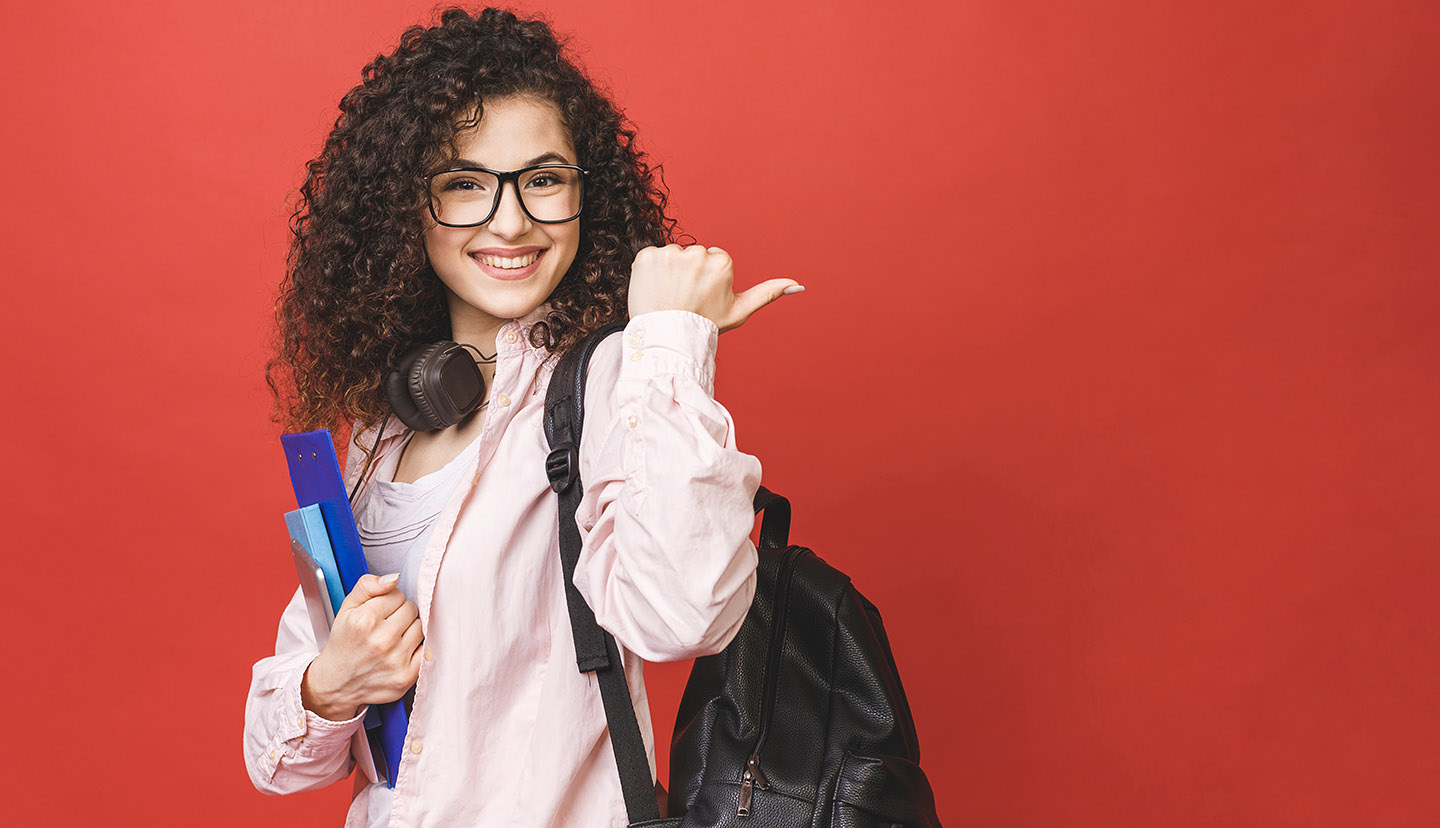 teen with books pointing back smiling